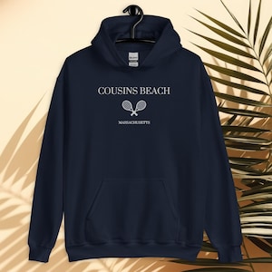 Peut inclure: Sweat-shirt à capuche bleu marine avec un graphique blanc de deux raquettes de tennis croisées et le texte "COUSINS BEACH MASSACHUSETTS".