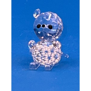 May include: A clear crystal figurine of a bear sitting with its paws outstretched. The bear has black eyes and a detailed, faceted body.