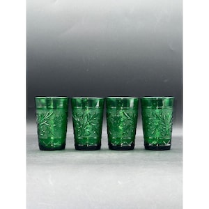 May include: Four green drinking glasses with a detailed leaf pattern. The glasses are made of a transparent material and have a classic design. The glasses are arranged in a row, showcasing their intricate details.