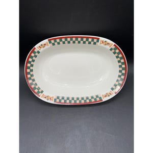 May include: White oval serving dish with a red and green checkered border. The dish has a simple design with a clean, bright appearance. The border features a repeating pattern of red and green squares, adding a touch of color.