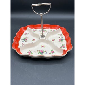 Pode incluir: Um prato de servir de cerâmica branca com uma borda vermelha e um padrão floral. O prato é dividido em quatro seções e tem uma alça de metal.