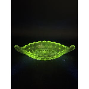 May include: A neon green, oval-shaped glass dish with a scalloped rim and two handles. The dish features a starburst design in the center and diamond-shaped patterns along the sides. The dish is likely vintage.
