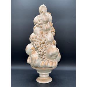 Puede incluir: Una escultura decorativa de cerámica con forma de topiario de frutas, que presenta una disposición apilada de manzanas, peras y uvas. La pieza tiene un acabado en esmalte color crema con detalles en oro metálico que resaltan las texturas.