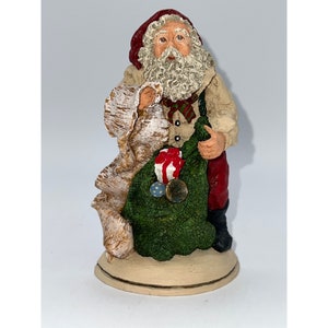 May include: A Santa Claus figurine holding a sack filled with gifts. He is wearing a red hat, white beard, and a red and white striped shirt. The figurine is made of painted ceramic and is approximately 10 inches tall.