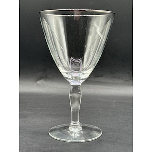 May include: A clear, stemmed glass with a wide, conical bowl and a delicate, etched design. The glass has a thin stem and a circular base. The rim of the glass is smooth. The glass is likely used for serving beverages.