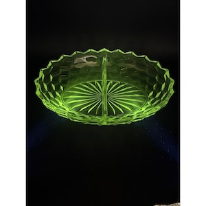 May include: A divided, oval-shaped, vintage glass serving dish. The dish is a bright, neon green color and features a geometric diamond pattern on the outer rim. The interior has a sunburst design. The dish is approximately 10 inches long.