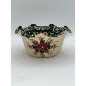 以下が含まれることがあります： 縁が波打った小さな白い陶器のボウル。ボウルは緑と白の斑点模様の釉薬と、赤いバラと緑の葉の入った花柄で飾られています。