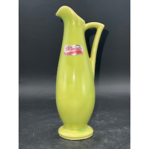 Puede incluir: Una jarra de cerámica verde con una etiqueta plateada que dice "Shawnee, Zanesville, Ohio".