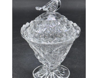 May include: A clear glass candy dish with a lid and a bird-shaped handle. The dish has a pedestal base and a diamond-cut pattern on the lid. The bowl has a floral design. The dish is likely vintage.