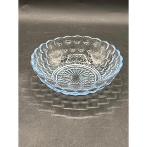 May include: A light blue glass bowl with a scalloped rim and a textured, bubble-like pattern. The bowl's interior features a radial design. This vintage bowl is suitable for serving snacks or as a decorative piece.