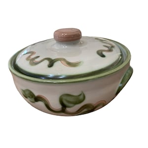 May include: A white ceramic casserole dish with a lid. The dish has a green and pink floral design. The lid has a pink knob.