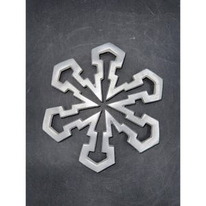 May include: A silver-colored snowflake ornament with six symmetrical arms. Each arm has a unique geometric design, with a central hub and a dark gray background.