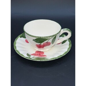 Puede incluir: Una taza de té y un platillo de cerámica blanca con un borde verde y un diseño de cerezas. Las cerezas son rojas y tienen hojas verdes.
