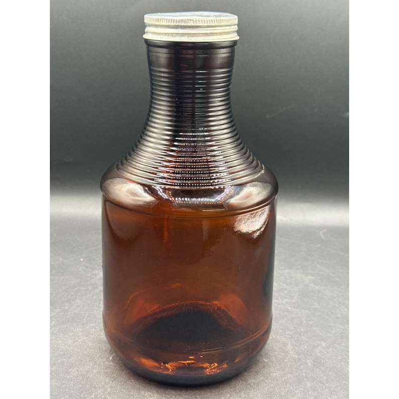 May include: A vintage brown glass bottle with a ribbed neck and a silver metal cap. The bottle has a rounded body and a dark amber color, suggesting it may be an old medicine or beverage container.