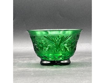 Op de afbeelding: Een groene glazen kom met een bloemmotief. De kom heeft een ronde basis en een uitlopende rand. Het bloemmotief is in reliëf op de buitenkant van de kom aangebracht. De kom is gemaakt van transparant groen glas.