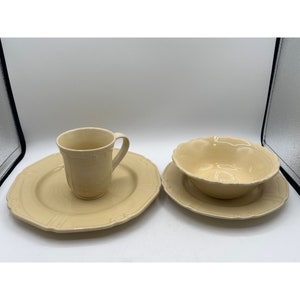 Puede incluir: Un juego de vajilla de cerámica de color crema, que incluye una taza, un tazón y un plato. La vajilla tiene un diseño simple y elegante con un sutil patrón en relieve.