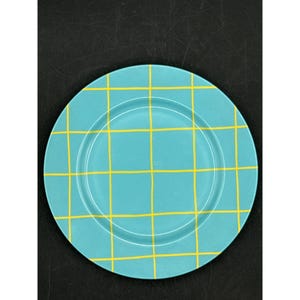 May include: A round, turquoise plate with a yellow grid pattern. The plate has a slightly raised rim and a smooth surface. The grid pattern is evenly spaced and covers the entire surface of the plate. The plate is likely for serving food.