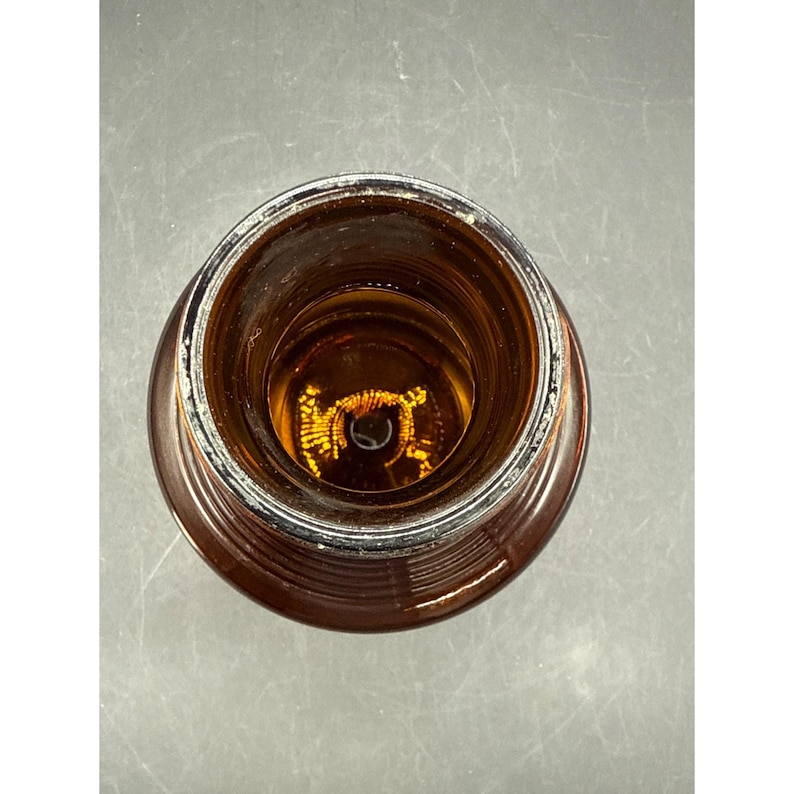 May include: An overhead view of a brown glass bottle. The bottle has a wide, circular opening and a ridged exterior. The interior of the bottle is visible, with a light source reflecting off the glass.
