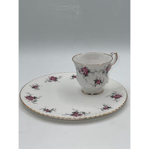 Puede incluir: Juego de taza y platillo de té blanco con un diseño floral de rosas rosas. La taza y el platillo tienen bordes dorados. El juego está sobre un fondo blanco. La taza está diseñada para unos 150 ml.