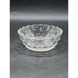 Op de afbeelding: Een heldere glazen kom met een geschulpte rand en een textuur, honingraatachtig patroon aan de zijkanten. De ronde kom staat op een donkere ondergrond, wat het transparante ontwerp benadrukt. Deze decoratieve kom is geschikt voor het serveren van snacks of het presenteren van kleine items.