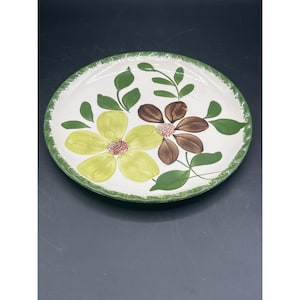 May include: A white ceramic plate with a green rim and a floral design. The flowers are yellow, brown, and green.