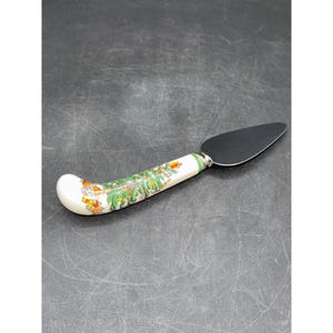 May include: A cake server with a stainless steel blade and a white handle. The handle is decorated with a green and gold Christmas tree design. The handle has a curved shape for easy use.