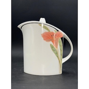 May include: White ceramic pitcher with a curved handle and a floral design. The pitcher features a stylized red flower with green leaves.