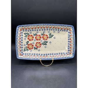 May include: Rectangular ceramic serving platter with a floral design. The platter features a cream-colored base with red and yellow flowers, green leaves, and blue accents. The border is blue with red and orange details.