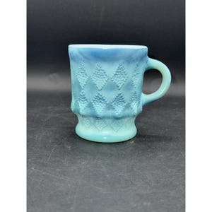 May include: A vintage blue glass mug with a handle. The mug features a diamond pattern and a light blue color gradient. The mug is made of glass and is suitable for hot or cold beverages.
