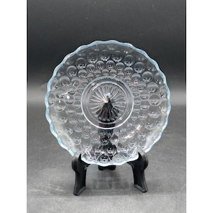 May include: Clear glass plate with a bubble pattern and a scalloped edge. The plate has a raised centre and is displayed on a black stand. The plate is likely for serving desserts or appetizers.