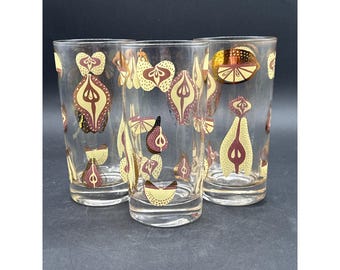 Könnte beinhalten: Drei transparente Trinkgläser mit modernem Design aus der Mitte des Jahrhunderts. Die Gläser weisen ein sich wiederholendes Muster aus stilisierten Früchten in Gold-, Braun- und Burgundertönen auf. Die Gläser sind zylindrisch und scheinen aus Glas zu sein.