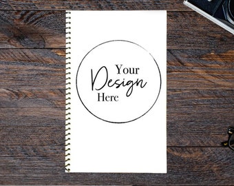 May include: A white spiral bound notebook with a black circle and the text "Your Design Here" on a wooden surface.