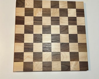 May include: A wooden chessboard with a checkerboard pattern of light and dark wood squares.