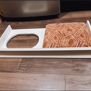 以下が含まれることがあります： 白木のペットベッドで、取り外し可能なクッションが付いています。クッションは茶色と白の幾何学模様です。