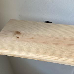 May include: A plain, light wood shelf with rounded edges. The shelf is mounted to a wall.