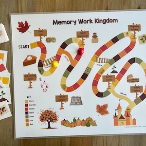 Puede incluir: Un tablero de juego colorido con un camino sinuoso, que presenta un castillo, un huerto de calabazas y una llave con cuadrados de diferentes colores que representan materias como historia, geografía e inglés. El tablero se titula "Memory Work Kingdom".