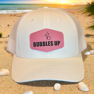 May include: White trucker hat with a pink leather patch that says "Bubbles Up" and a small graphic of bubbles.