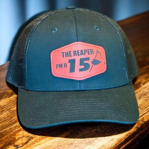 May include: A black and red trucker hat with a patch that says "THE REAPER PM II 15" with a scythe and arrow graphic.