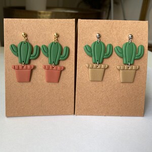 May include: Two pairs of green cactus earrings with brown pots. The earrings on the left have gold hooks and the earrings on the right have silver hooks.