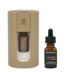 Op de afbeelding: Een beige diffuser met een heldere glazen fles erin en de tekst "DOT ME WELL" aan de voorkant. Een klein bruin flesje met een zwarte druppelaar en de tekst "DOT ME WELL LAVENDER DIFFUSER ESSENTIAL OIL BLEND" op het etiket.