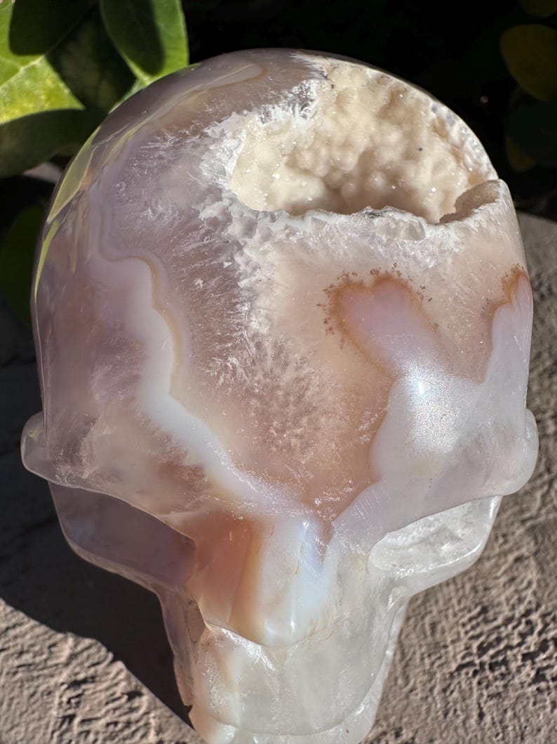 Puede incluir: Un cr&aacute;neo de &aacute;gata blanco y rosa con una gran cavidad de geoda de cristal blanco abierta. El cr&aacute;neo est&aacute; tallado en una piedra de &aacute;gata natural y tiene un acabado liso y pulido.