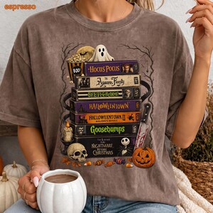 May include: A brown mineral-washed t-shirt featuring a graphic print of a stack of VHS tapes titled Hocus Pocus, The Addams Family, Beetlejuice, Halloweentown, Halloweentown II, Goosebumps, and The Nightmare Before Christmas, with a ghost, skull, and pumpkin.