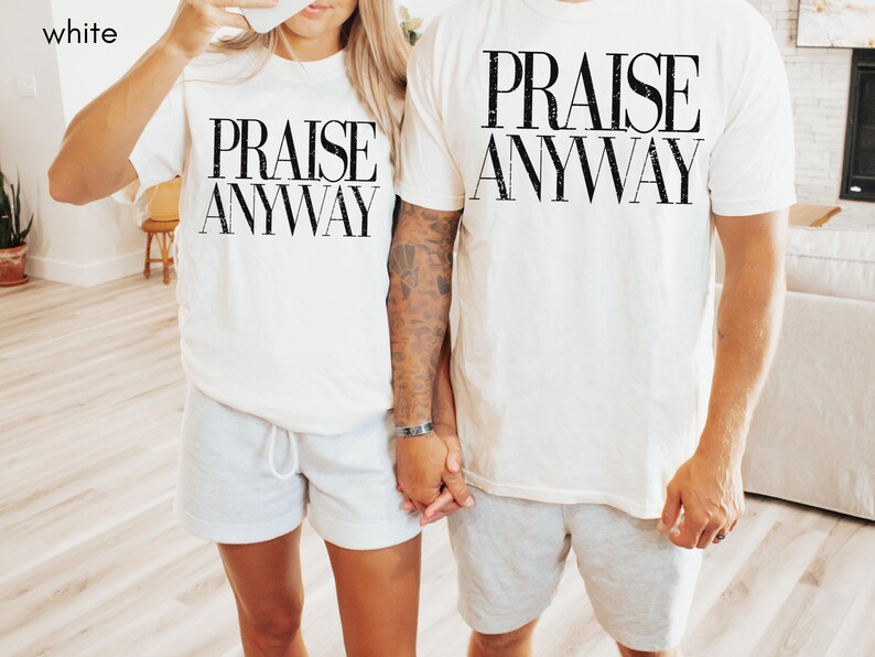 May include: White t-shirts with the text "PRAISE ANYWAY" in black, worn with gray shorts. The image shows two people holding hands, wearing matching outfits. The word "white" is in the top left corner.
