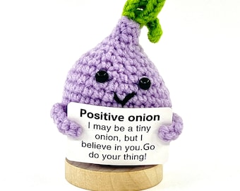 May include: A crocheted purple onion with a green stem holding a sign that reads "Positive onion I may be a tiny onion, but I believe in you. Go do your thing!"