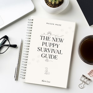 May include: A spiral-bound notebook titled "The New Puppy Survival Guide" with paw print accents, a puppy illustration, and the author's name, Marie Luca. The notebook is on a white desk with a laptop, glasses, pen, and a cup of coffee.