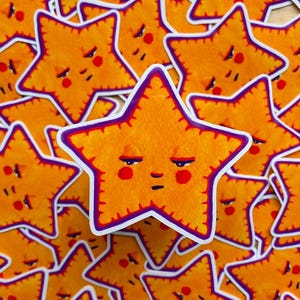 May include: A stack of yellow star-shaped stickers with a purple outline and a grumpy face. Each star has a red nose and red cheeks.