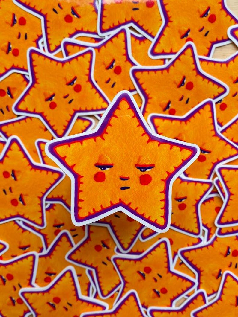 May include: A stack of yellow star-shaped stickers with a purple outline and a grumpy face. Each star has a red nose and red cheeks.