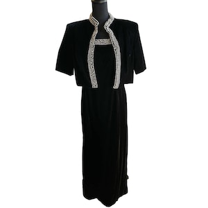 May include: A black velvet dress with a matching short-sleeved jacket. The dress has a beaded neckline and a slit in the skirt.