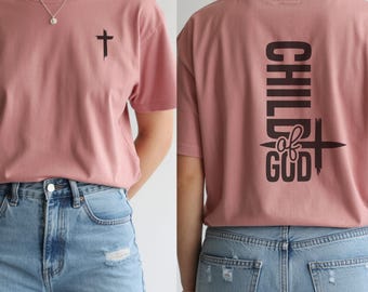 May include: Dusty rose t-shirt with a black cross graphic on the front and the words "CHILD of GOD" on the back. The shirt is paired with light blue denim jeans. The cross graphic is slightly distressed.