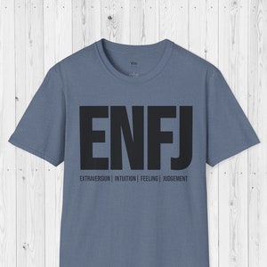 Può includere: Una maglietta blu con le lettere ENFJ stampate in nero. Il testo "EXTRAVERSION | INTUITION | FEELING | JUDGEMENT" è stampato sotto le lettere.